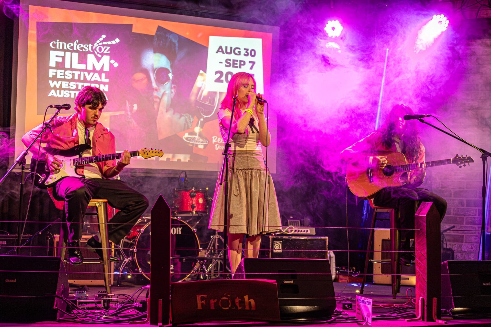 Band Performing On An Indoor Stage Under Pink Lights.