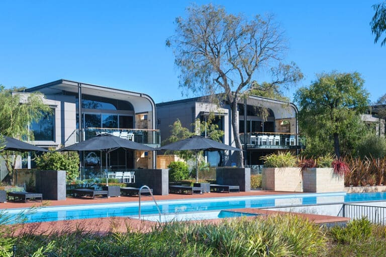 Double Story Hotel Villas Behind A Pool Area.