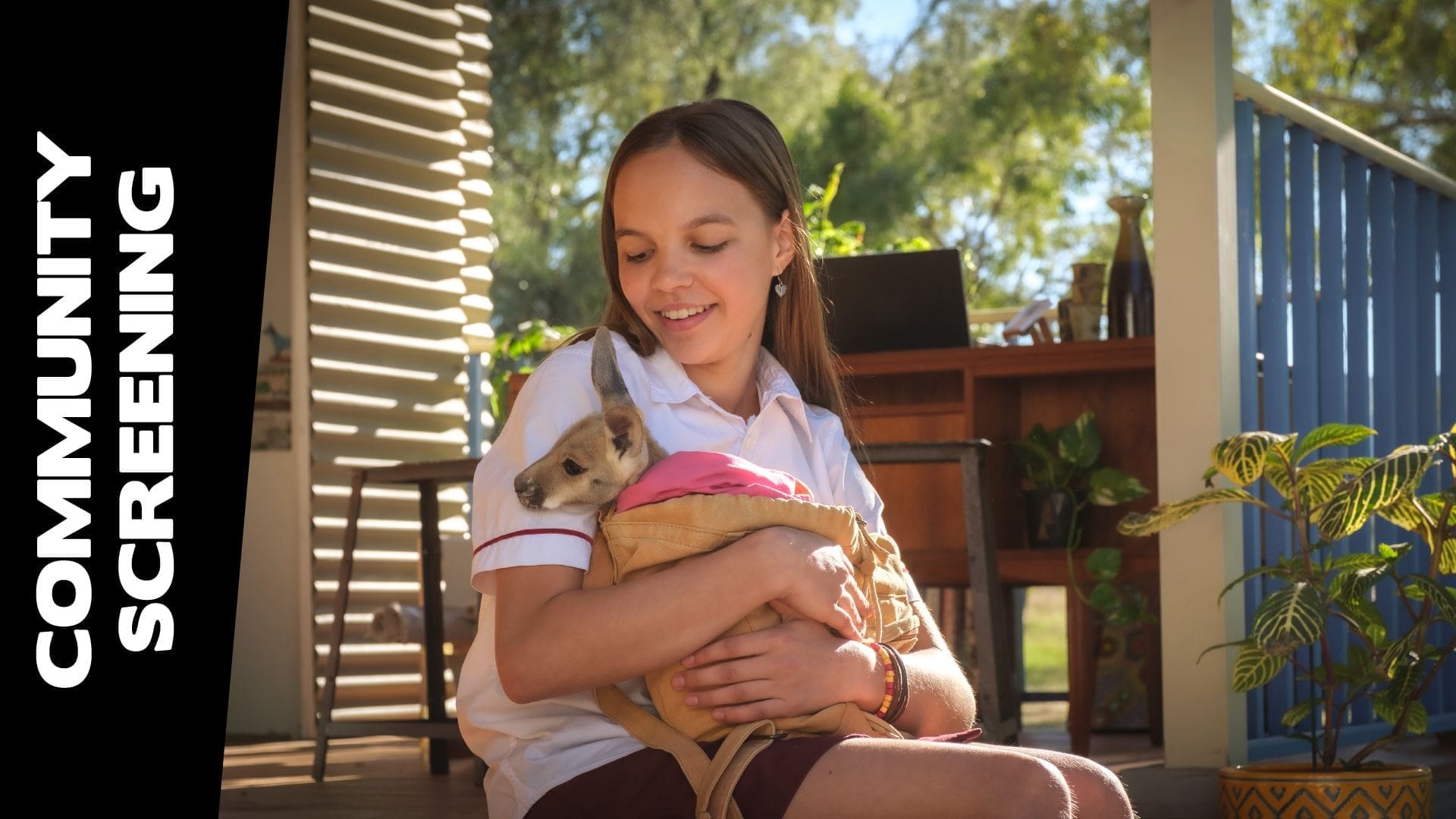 Young Girl Sitting Outside, Holding A Joey Wrapped In A Blanket.